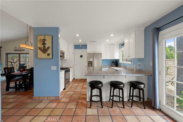 kitchen with a sink, a peninsula, stainless steel appliances, white cabinetry, and a kitchen bar