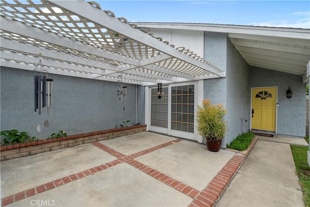 doorway to property with stucco siding, a pergola, and a patio area