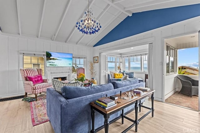 living room with a warm lit fireplace, an inviting chandelier, light wood-style flooring, and vaulted ceiling with beams