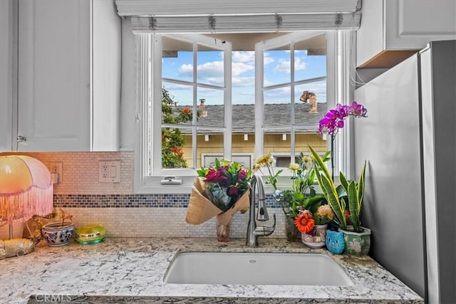 room details featuring freestanding refrigerator, backsplash, white cabinets, and a sink