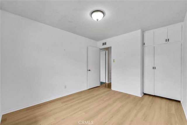 unfurnished bedroom featuring light wood-style flooring, a closet, and baseboards