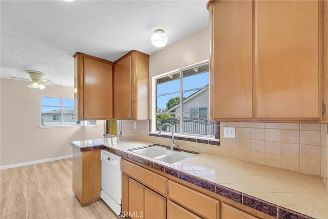 kitchen with a sink, white dishwasher, decorative backsplash, a textured ceiling, and light wood-style flooring