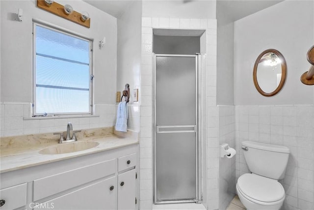 bathroom with tile walls, a stall shower, toilet, vanity, and wainscoting