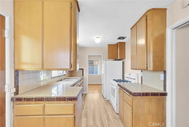kitchen featuring a sink, white range with gas stovetop, decorative backsplash, light wood finished floors, and tile countertops