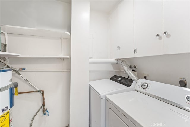 clothes washing area featuring washing machine and dryer, water heater, and cabinet space