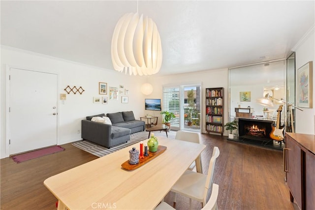 dining area featuring dark wood-type flooring, a warm lit fireplace, and ornamental molding