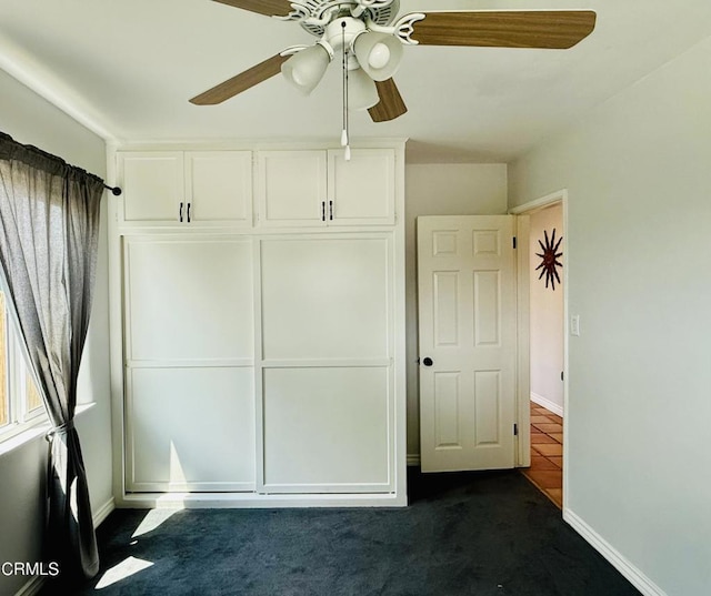 unfurnished bedroom featuring ceiling fan, baseboards, and dark carpet