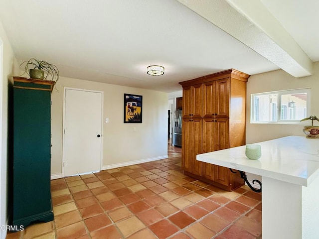 kitchen featuring a peninsula, stainless steel fridge, brown cabinets, baseboards, and light tile patterned flooring