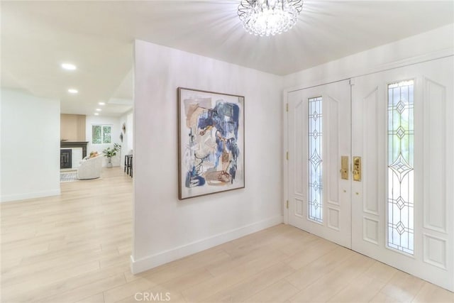 foyer featuring baseboards, wood finished floors, a chandelier, recessed lighting, and a brick fireplace