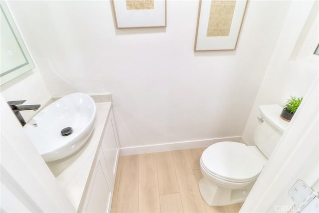 half bathroom featuring vanity, wood finished floors, toilet, and baseboards