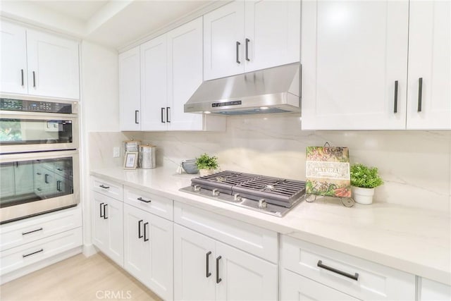 kitchen with under cabinet range hood, stainless steel appliances, backsplash, and white cabinets