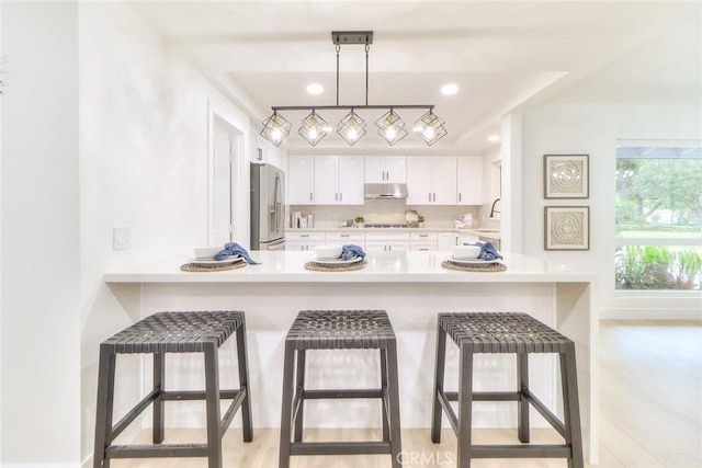 kitchen featuring stainless steel fridge with ice dispenser, under cabinet range hood, a sink, light countertops, and white cabinetry