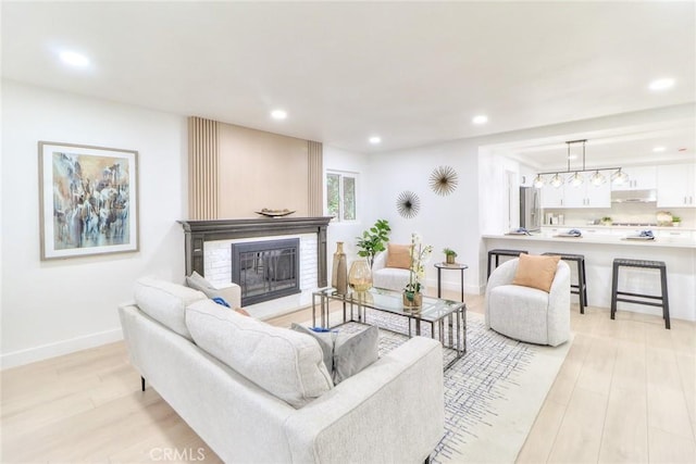 living room featuring light wood-type flooring, a glass covered fireplace, recessed lighting, and baseboards