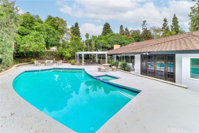 view of pool with a patio, a pool with connected hot tub, view of wooded area, and a pergola