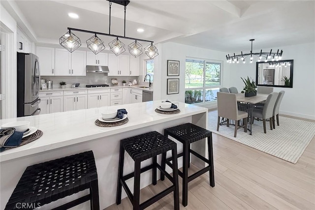 kitchen with stainless steel appliances, under cabinet range hood, a sink, a chandelier, and light countertops