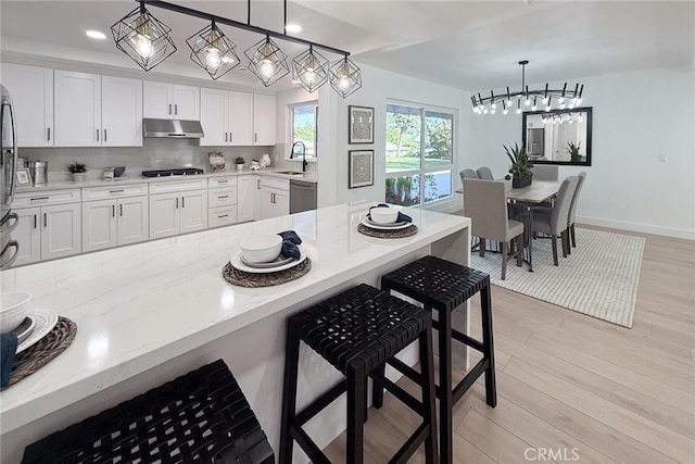 kitchen with under cabinet range hood, a breakfast bar area, white cabinets, light wood finished floors, and decorative light fixtures