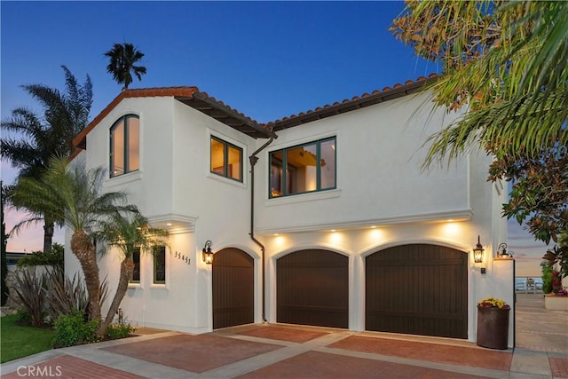 mediterranean / spanish-style house featuring an attached garage, stucco siding, and decorative driveway