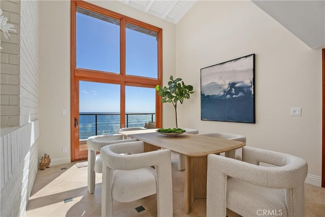 dining space featuring light tile patterned floors, a water view, baseboards, and high vaulted ceiling