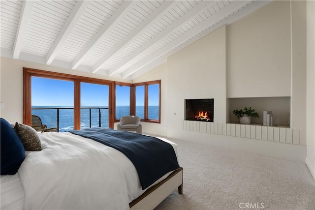 bedroom with a large fireplace, a water view, lofted ceiling with beams, and carpet