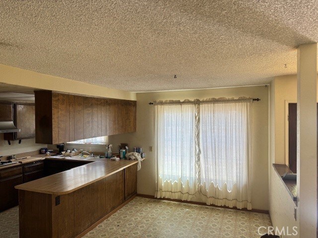14122 Pawnee Rd, Apple Valley, CA 92307 - kitchen with a peninsula, under cabinet range hood, and a textured ceiling