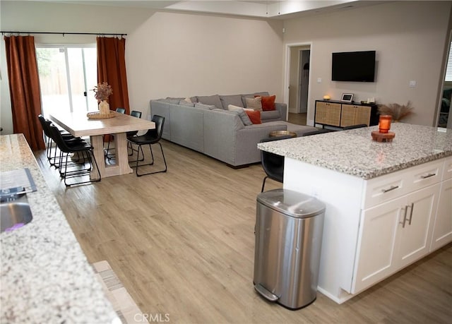kitchen featuring white cabinetry, light stone counters, open floor plan, and light wood-type flooring