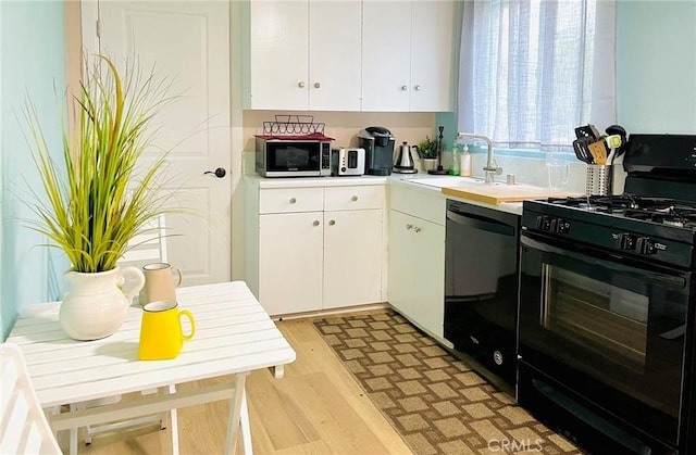 kitchen featuring light wood finished floors, a sink, white cabinets, black appliances, and light countertops