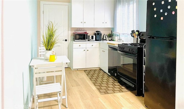 kitchen with white cabinetry, black appliances, light wood-style flooring, and a sink