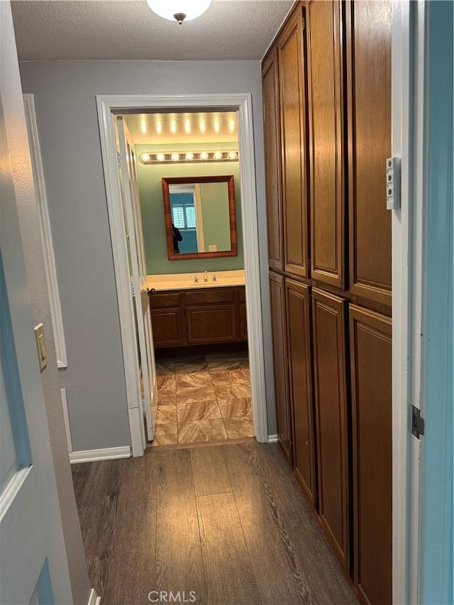 hall featuring a sink, a textured ceiling, baseboards, and wood finished floors