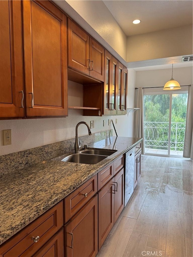 kitchen featuring light wood finished floors, a sink, brown cabinetry, stainless steel dishwasher, and visible vents