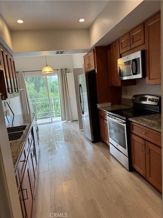 kitchen with light wood finished floors, dark stone counters, stainless steel appliances, brown cabinetry, and visible vents