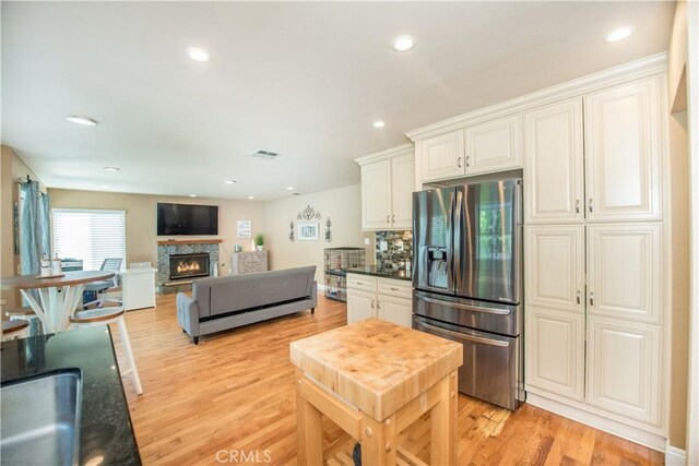 3251 Mountainside Dr, Corona, CA 92882 - kitchen featuring stainless steel refrigerator with ice dispenser, light wood-type flooring, a sink, a stone fireplace, and white cabinets