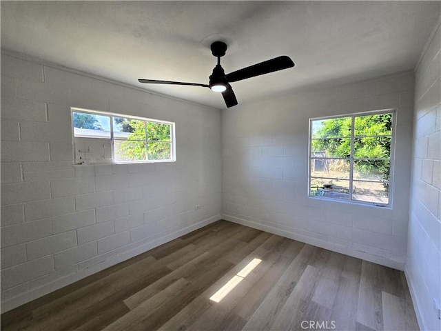 empty room featuring ceiling fan, concrete block wall, and wood finished floors