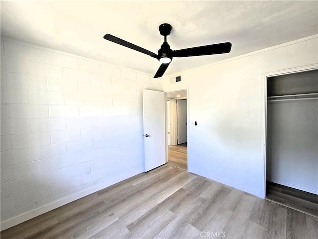 unfurnished bedroom featuring a closet, wood finished floors, visible vents, ceiling fan, and concrete block wall