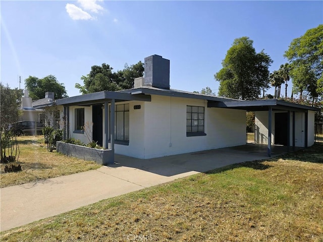 ranch-style house with concrete driveway, a front yard, a chimney, and a carport