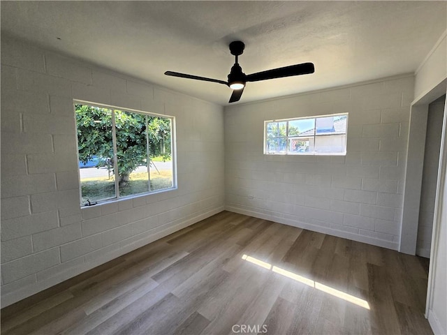 empty room featuring concrete block wall, wood finished floors, and ceiling fan