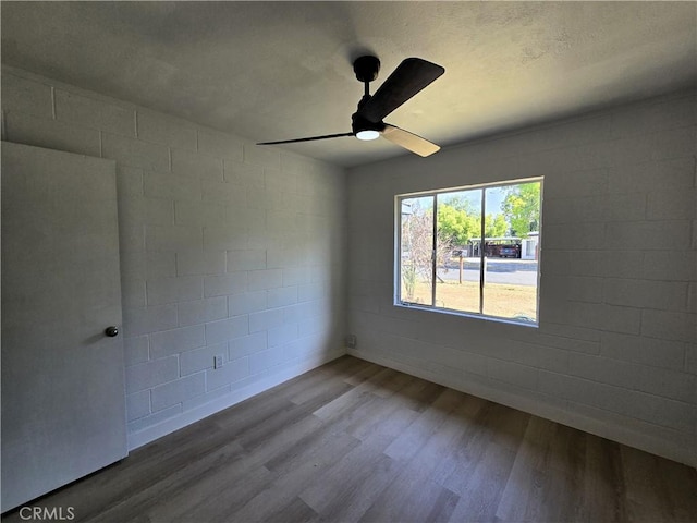 spare room featuring concrete block wall, a ceiling fan, and wood finished floors