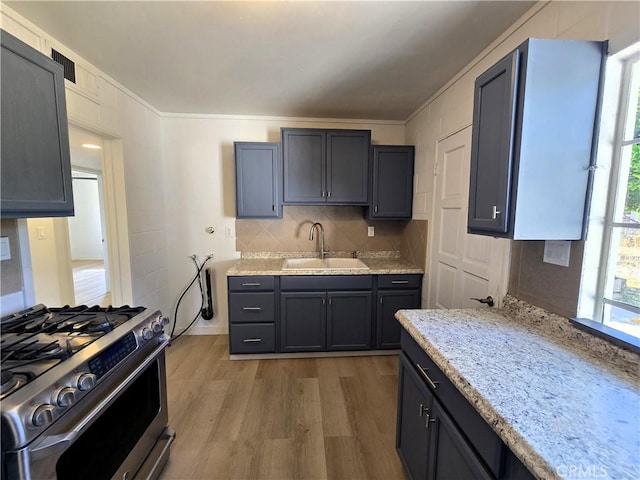 kitchen featuring a sink, tasteful backsplash, light wood-type flooring, stainless steel gas range, and light stone countertops