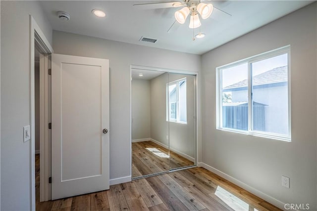unfurnished bedroom featuring hardwood / wood-style flooring, a closet, visible vents, ceiling fan, and baseboards