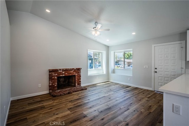 unfurnished living room featuring vaulted ceiling, ceiling fan, dark wood-style flooring, a brick fireplace, and baseboards