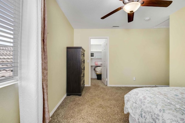 bedroom with a ceiling fan, a walk in closet, visible vents, baseboards, and light colored carpet