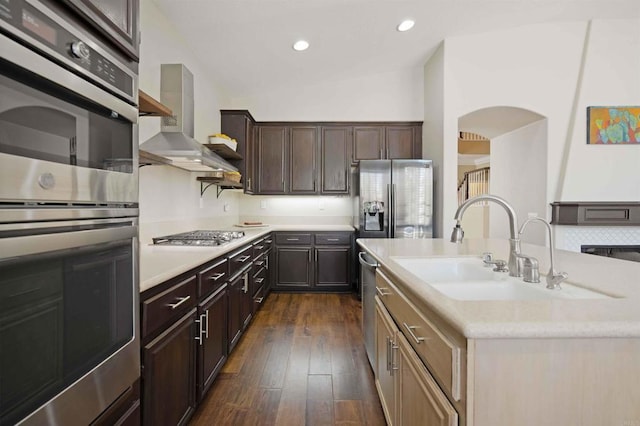 kitchen with a sink, wall chimney exhaust hood, appliances with stainless steel finishes, vaulted ceiling, and dark wood-style floors