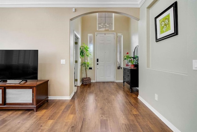 entrance foyer featuring ornamental molding, arched walkways, baseboards, and wood finished floors