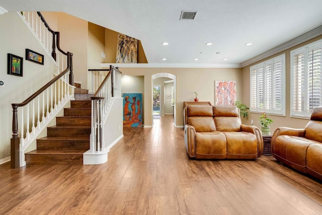 living room with wood finished floors, crown molding, visible vents, arched walkways, and stairs