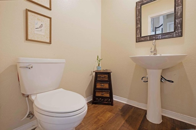 half bathroom featuring toilet, baseboards, a sink, and wood finished floors