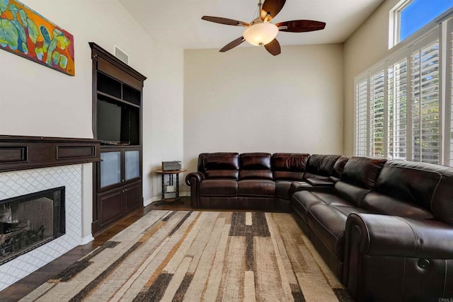 living room with a tile fireplace, wood finished floors, a ceiling fan, visible vents, and built in features
