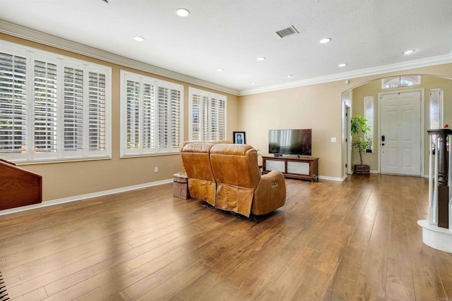 living area with arched walkways, baseboards, crown molding, and hardwood / wood-style flooring