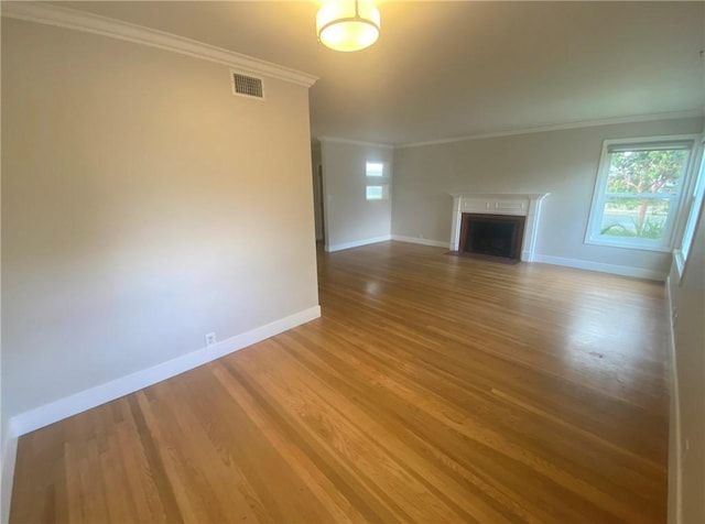 unfurnished living room with wood finished floors, a fireplace with flush hearth, crown molding, visible vents, and baseboards