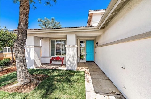 doorway to property featuring covered porch, a tiled roof, and stucco siding