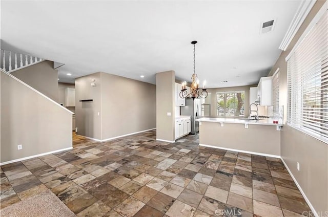 kitchen with a sink, a peninsula, white cabinetry, light countertops, and a notable chandelier
