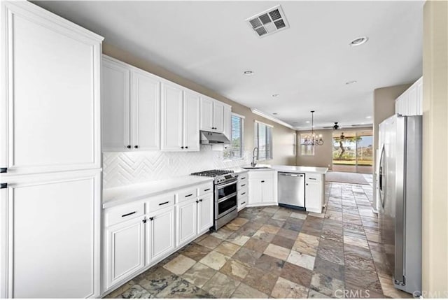 kitchen with under cabinet range hood, stone finish flooring, visible vents, a peninsula, and appliances with stainless steel finishes